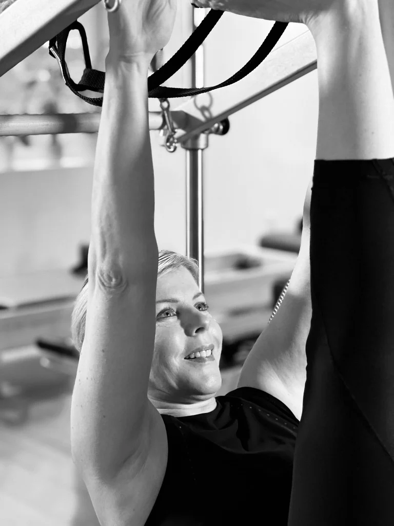 Julie practising Pilates with her arms raised toward the apparatus