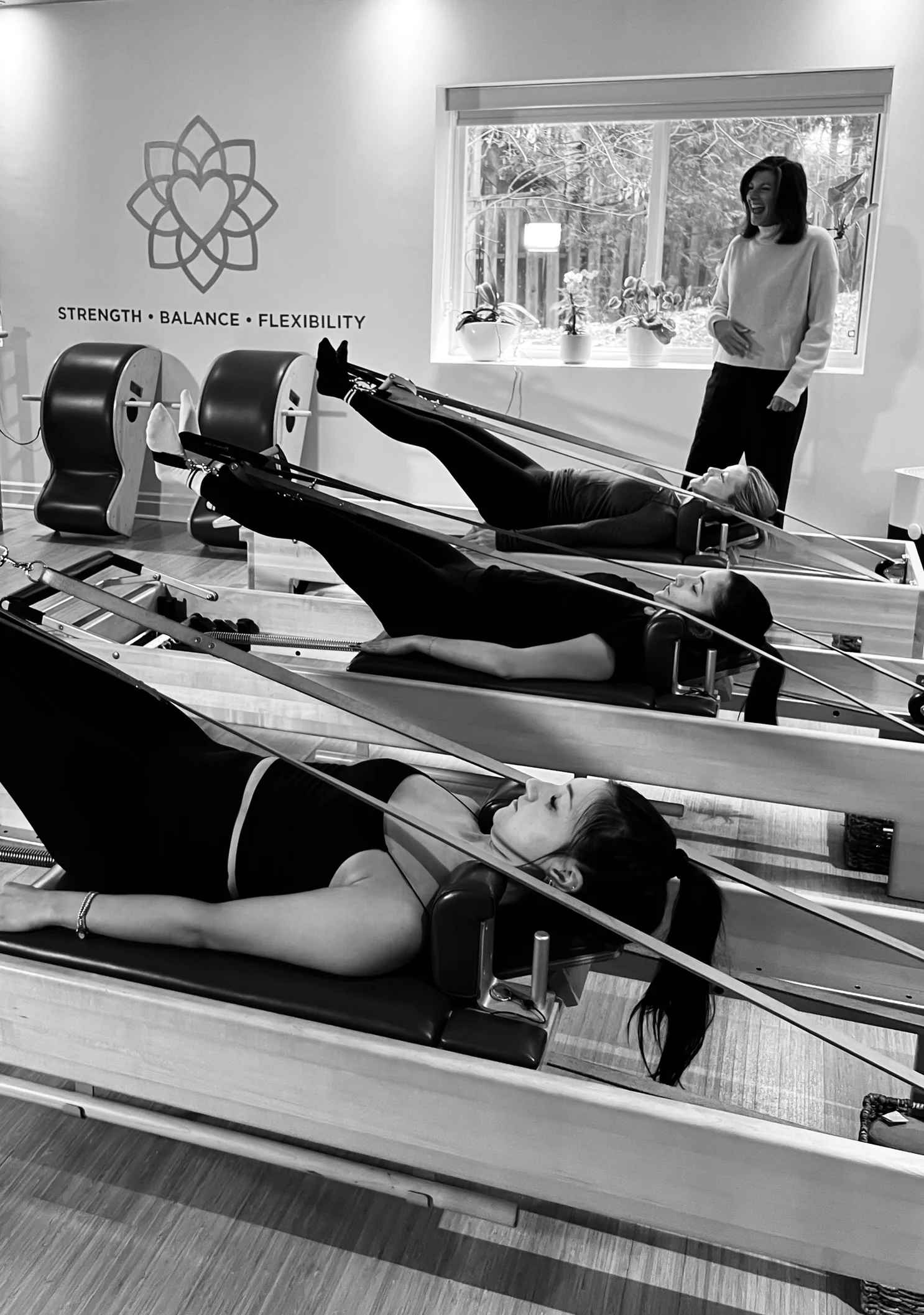 Kim teaching three clients using leg straps on Reformers during a small group Pilates class