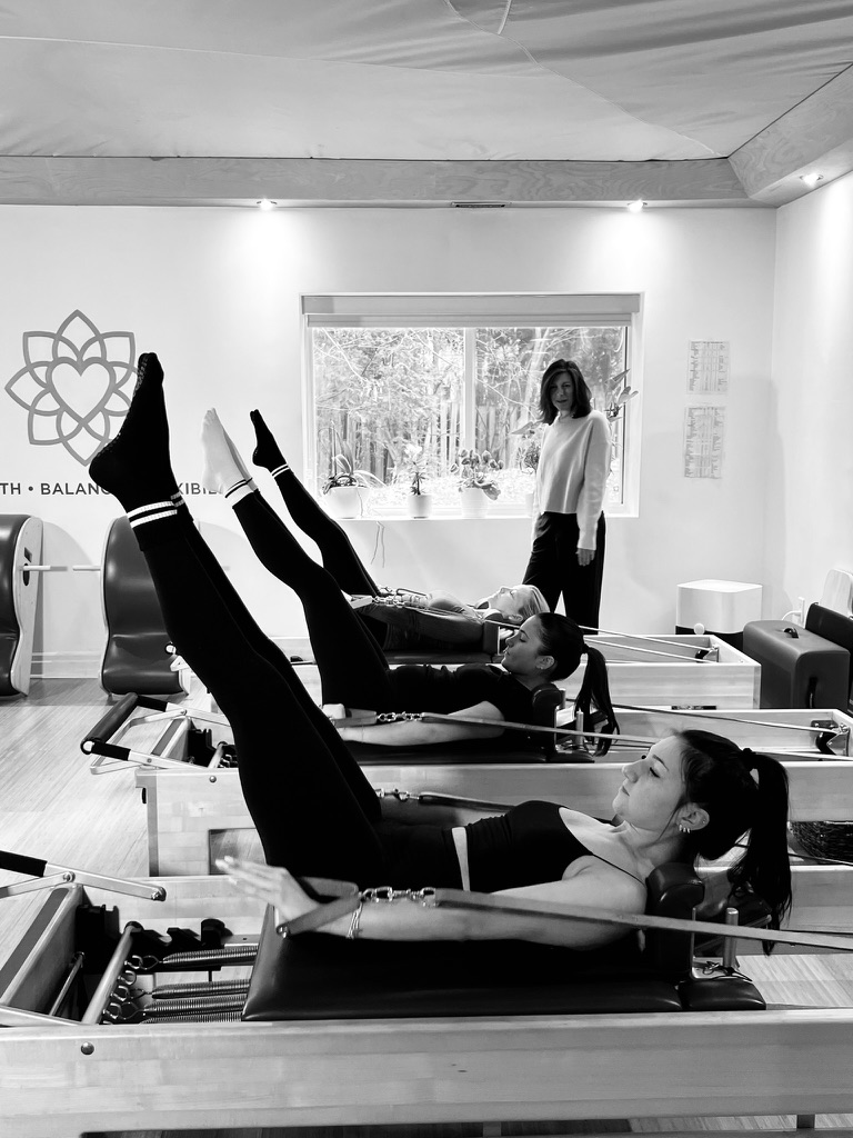 Instructor guiding a client on the Pilates Reformer machine