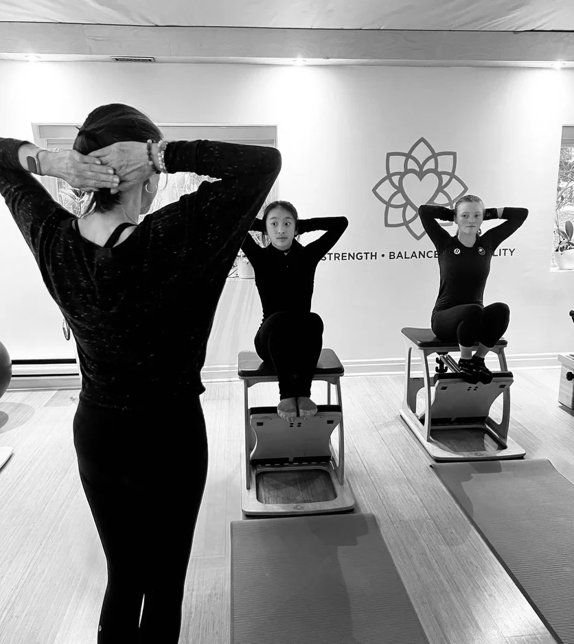 An instructor demonstrating an exercise to two clients seated on Pilates chairs