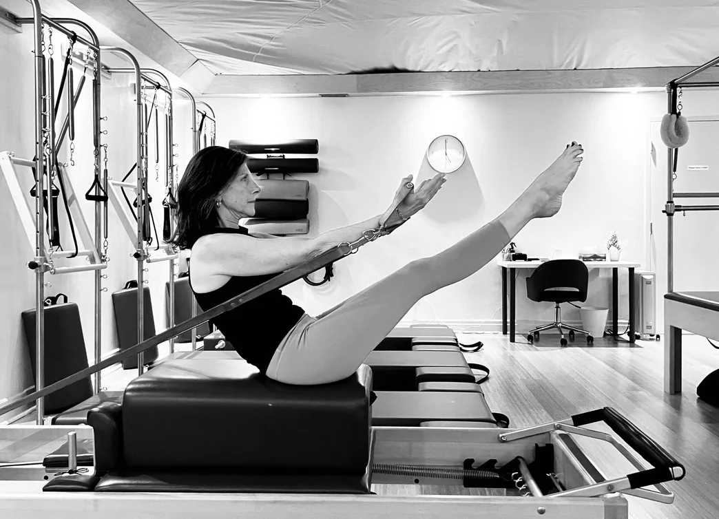 A woman balancing on a Reformer box with her arms and legs extended