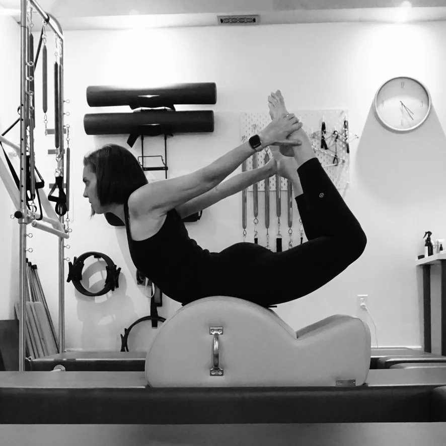 A woman arching over a spine corrector while holding her feet behind her