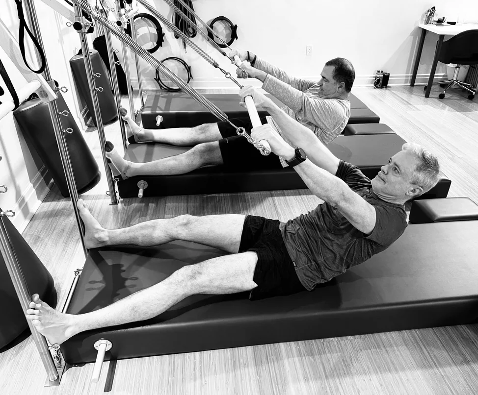 Two clients leaning back on Tower mats while holding spring bars