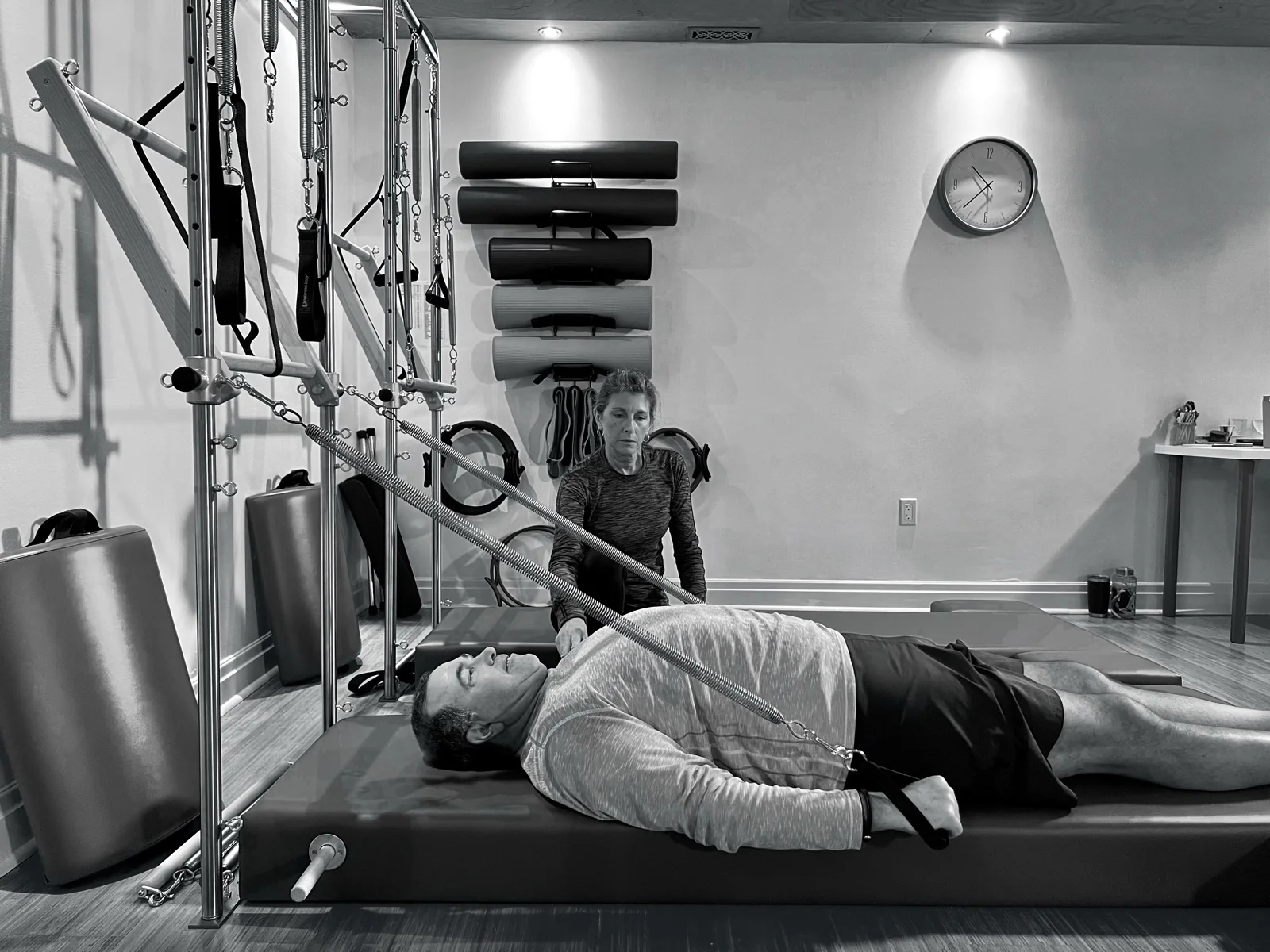 An instructor guiding a client lying on a Tower mat while using spring handles