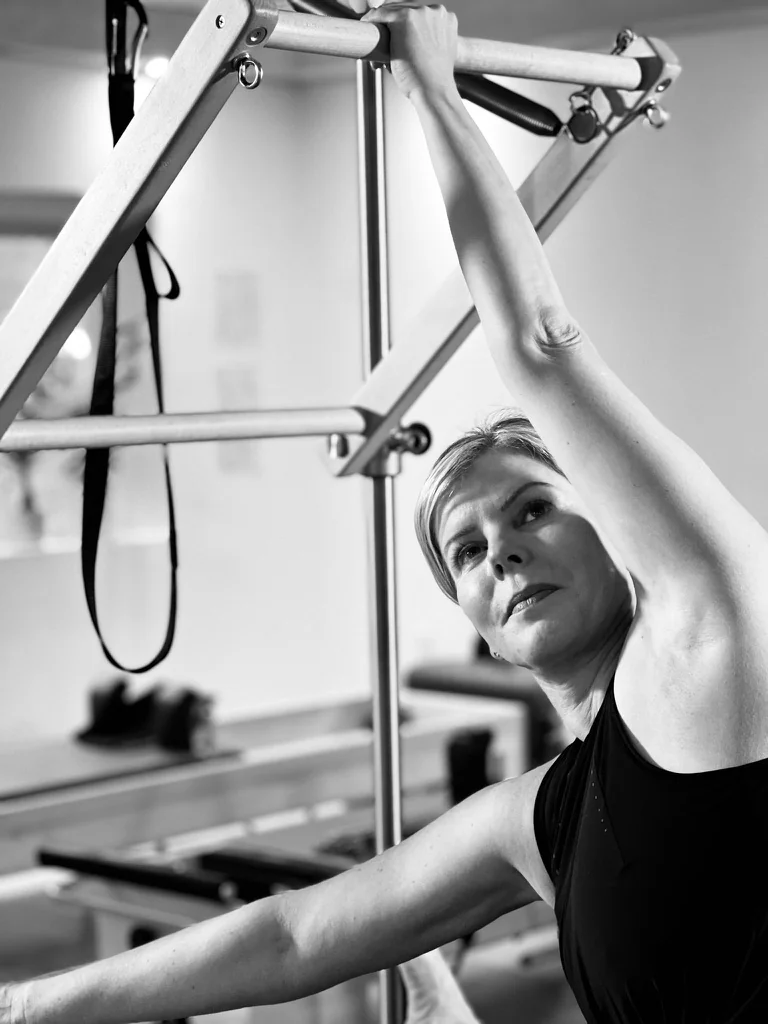 A woman stretching sideways with one arm reaching up to the Tower push-through bar